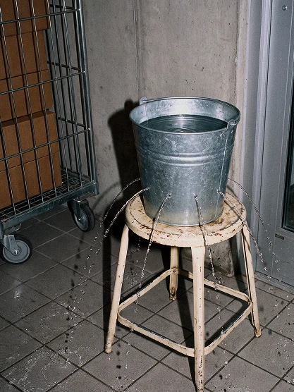 En metallhink fylld med vatten står på en pall och läcker vatten från flera små hål.