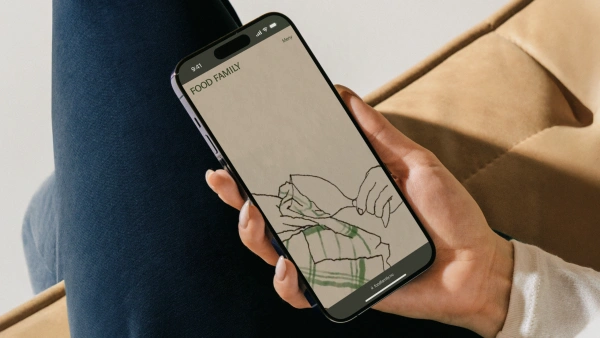 En kvinnlig hand håller en smartphone med Food Familys startsida