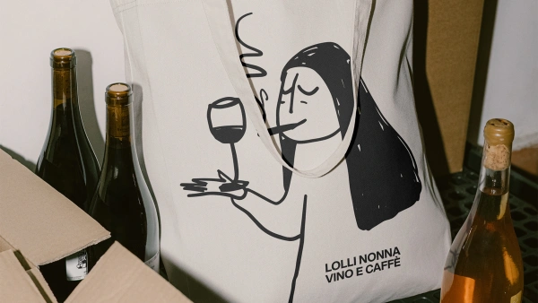 Tygkasse med Lolli Nonnas logga står på ett bord med vinflaskor